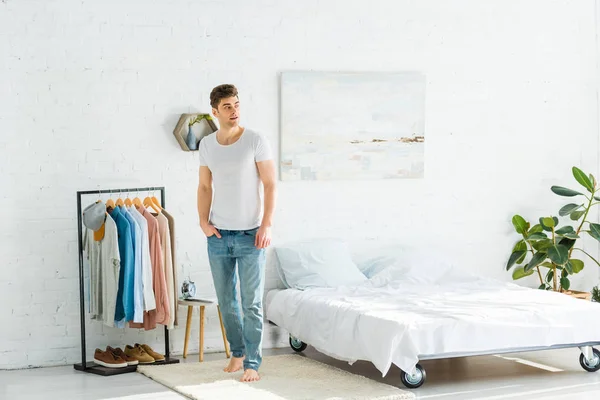 Handsome Man White Shirt Jeans Standing Bed Clothes Rack Bedroom — Stock Photo, Image