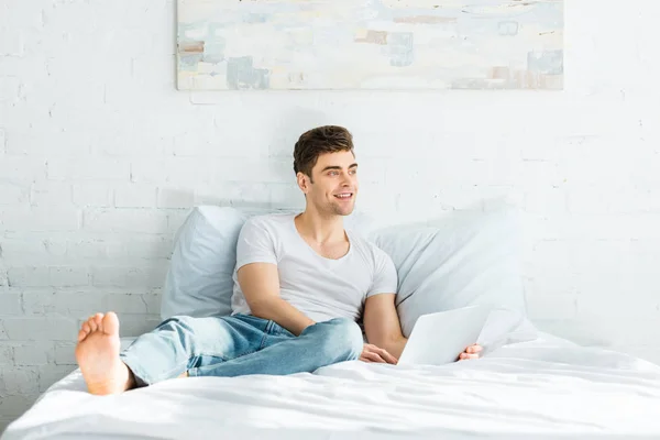 Handsome Man White Shirt Jeans Sitting Bed Laptop Smiling Bedroom — Stock Photo, Image