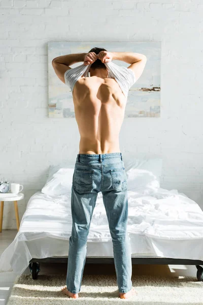 Hombre Jeans Pie Hacia Atrás Cerca Cama Quitándose Camiseta Blanca —  Fotos de Stock
