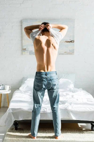 Homme Jeans Debout Vers Arrière Près Lit Enlever Shirt Blanc — Photo