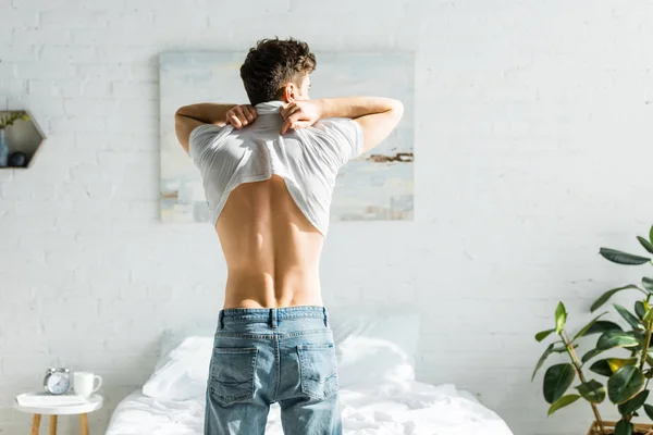 Człowiek Dżinsach Tyłu Stojąc Pobliżu Łóżka Startu Biały Shirt Sypialni — Zdjęcie stockowe