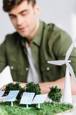selective focus of architect at table with windmill, trees, solar panels models in office clipart