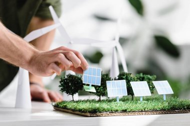 cropped view of man putting solar panels models on grass on table in office clipart