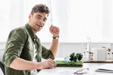 ağaçlar, çimenler, yel değirmenleri, binalar ve güneş panelleri modelleri ofis ile masada oturma mimar