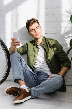 Yeşil tişörtlü smartphone, tuğla duvar ve bisiklet Office yakınında oturan tutan yakışıklı adam