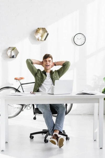英俊的商人在绿色衬衫坐在桌子与笔记本电脑和微笑在办公室 — 图库照片