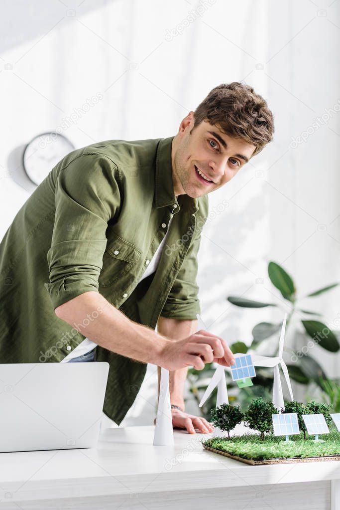 handsome man putting solar panels models on grass on table in office