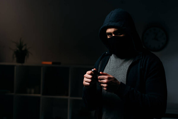 Burglar in mask standing in dark room and holding keys