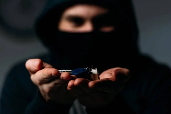 Thief in mask and hoodie showing keys at camera