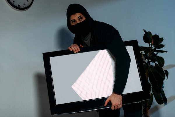 Robber in black mask stealing flat-screen tv with blank screen 