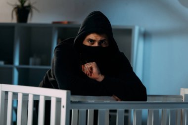 Siyah kıyafet ve maske ayakta beşik yanında endişeli çocuk hırsızı