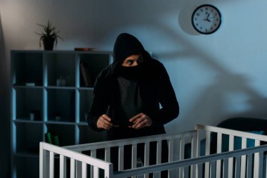 Siyah maske ayakta beşik ve alma resim endişeli çocuk hırsızı