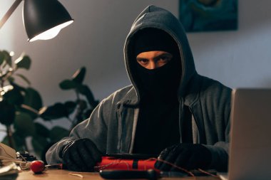 Terrorist in mask and hoodie making bomb in room clipart