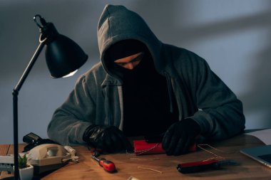Concentrated terrorist in leather gloves making bomb in room clipart
