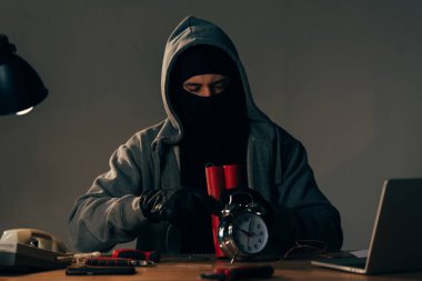 Concentrated terrorist in mask and black gloves making bomb clipart