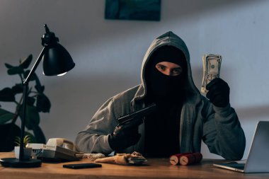 Terrorist in mask and gloves holding gun and dollar banknotes clipart