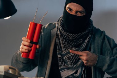 Aggressive terrorist pointing with finger at dynamite and looking at camera clipart