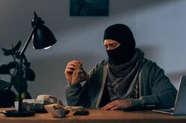 Oturma odasında ve küçük para çantası tutan maskeli üzgün terörist