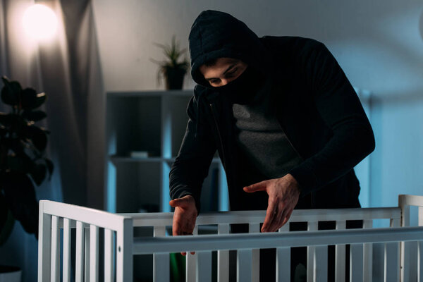 Преступник в маске и черной одежде похищает ребенка из кроватки
