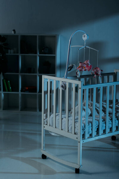 Детская кроватка с мобильным телефоном и шкафом стоит в темной комнате
