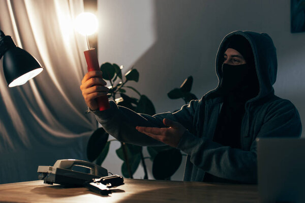 Pleased terrorist in mask holding lighted dynamite in room