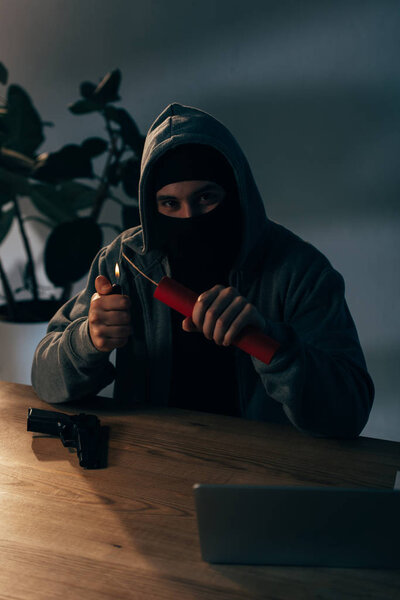 Хитрый террорист в маске, поджигающий динамит в темной комнате
