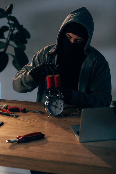 Concentrated terrorist in mask and gloves making bomb in room