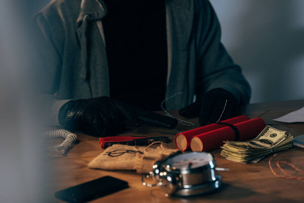 Обрезанный вид преступника в кожаных перчатках с пистолетом и динамитом
