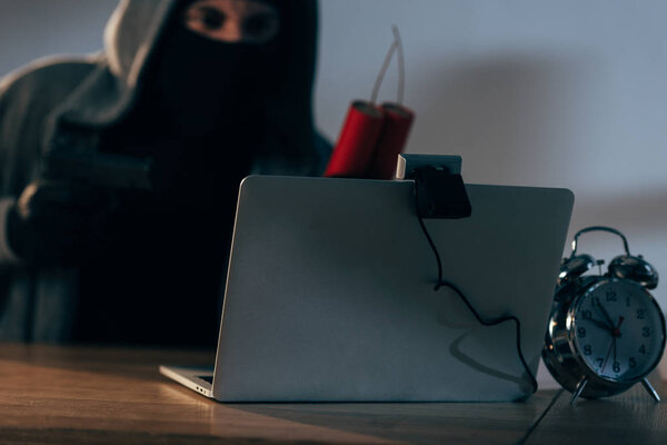 Terrorist in mask holding dynamite while using laptop in dark room
