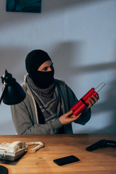 Terrorist in mask holding dynamite while sitting in dark room