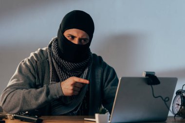 Webcam seyir ve dizüstü bilgisayar ekranında parmakla işaret eden maskeli terör