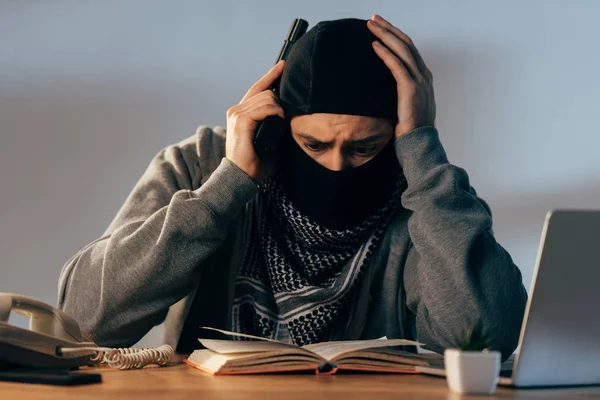 Besorgter Terrorist Mit Maske Berührt Kopf Beim Lesen Von Buch — Stockfoto