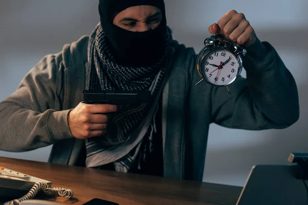 好斗的恐怖分子拿着枪和闹钟在桌旁 — 图库照片