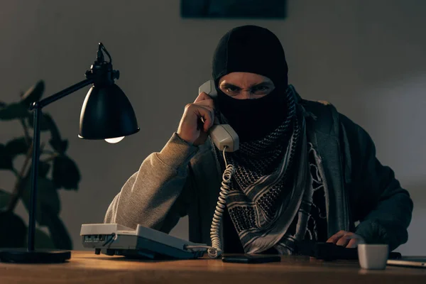Terrorista Furioso Máscara Sentado Mesa Com Lâmpada Falando Telefone — Fotografia de Stock
