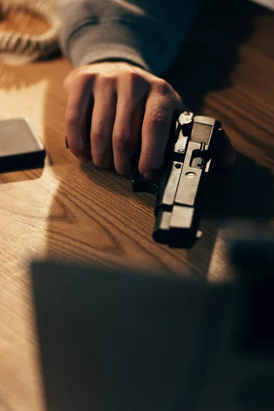Cropped view of criminal holding gun on wooden table