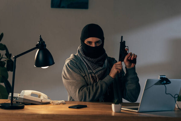 Преступник в черной маске смотрит в камеру и заряжает пистолет в комнате
