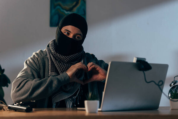 Criminal in black mask showing heart sign at webcam