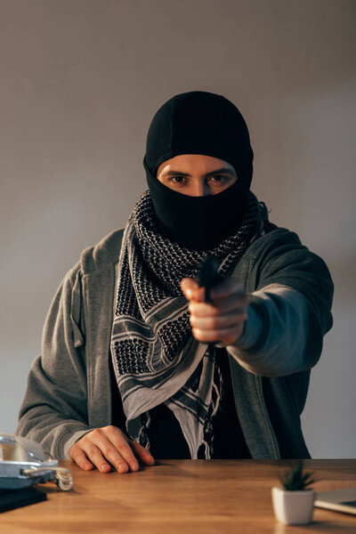 Concentrated criminal in black mask aiming gun at camera