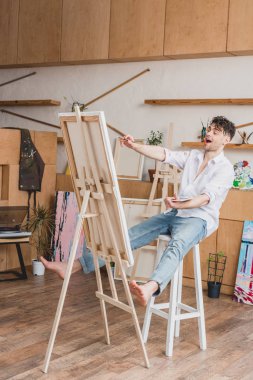 şövale tuval ile yüksek sandalye üzerinde oturan ressam