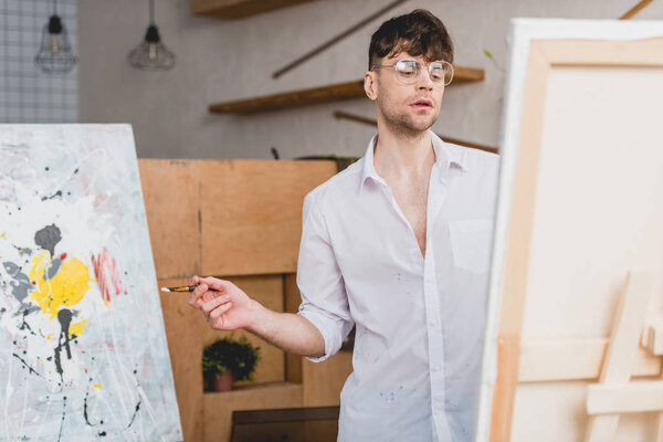 селективный фокус красивого художника с кистью, смотрящего на холст
