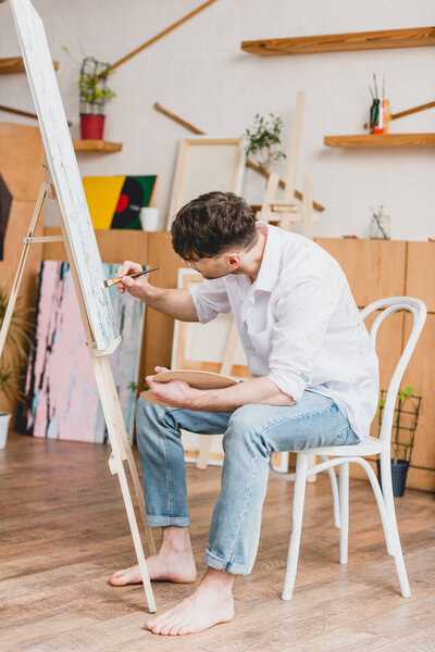 pensive artist in white shirt and blue jeans painting on canvas