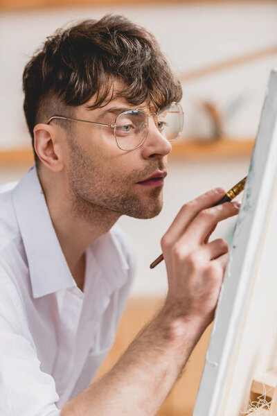 селективная направленность красивого художника в очках живопись на холсте
