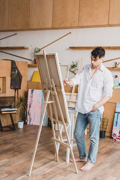 handsome artist in white shirt and blue jeans painting on canvas 