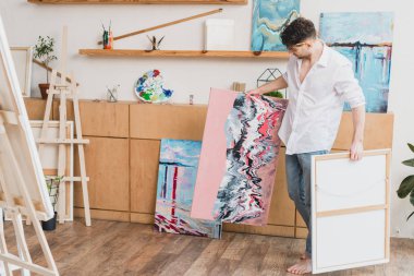 barefoot artist in white shirt and blue jeans carrying paintings in gallery clipart