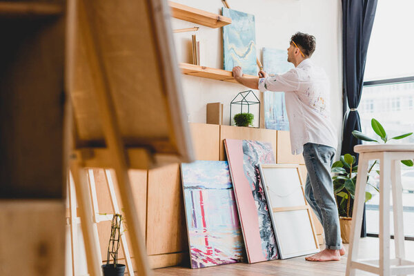 selective focus of artist in white shirt and blue jeans standing in light gallery