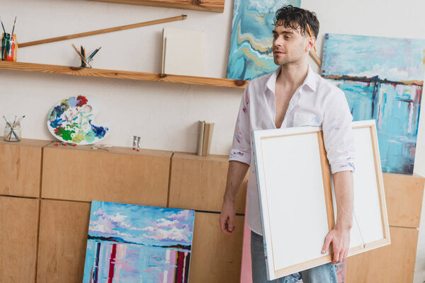 handsome artist in white shirt and blue jeans carrying canvas