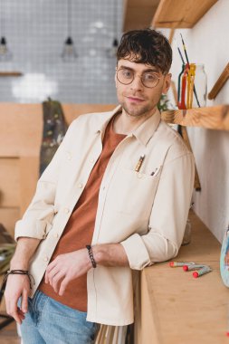 seçici odak resim stüdyoda ayakta ve kameraya bakarak gözlük yakışıklı sanatçının