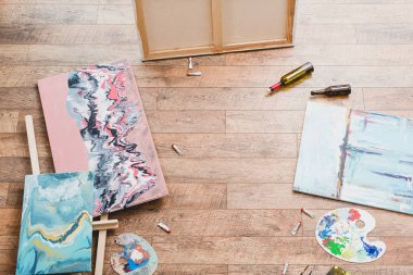 high angle view of paintings, draw utensils and empty bottles on wooden floor in painting studio clipart