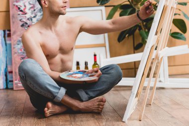 partial view of half-naked artist sitting on floor and painting picture  clipart