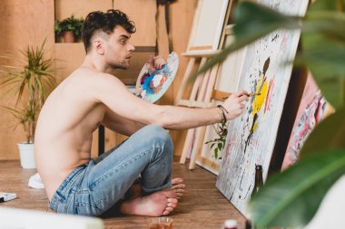 selective focus of thoughtful half-naked artist holding palette and painting picture clipart